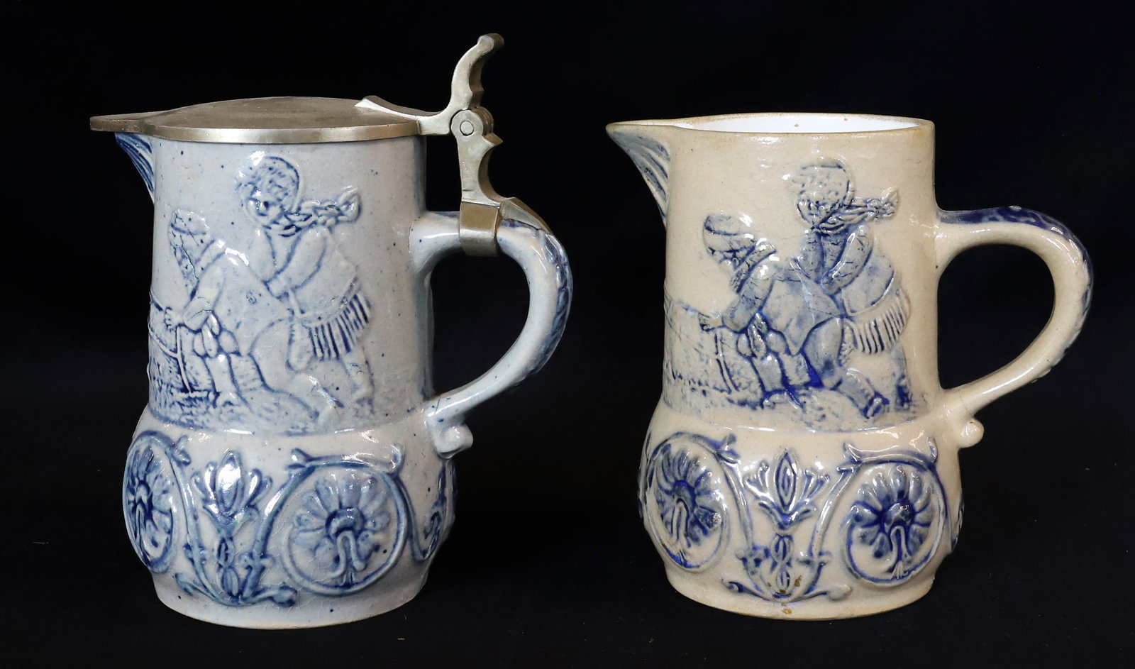 (2) STONEWARE DECORATED PITCHERS: ONE WITH PEWTER LID. BLUE HIGHLIGHTS ON BOTH. UNMARKED. ATTR. TO WHITE'S UTICA. 5" H. PLEASE READ CAREFULLY - ITEMS MUST BE PAID FOR THROUGH LIVE AUCTIONEERS OR WITH CASH OR CHECK IN PERSON - Terms fo