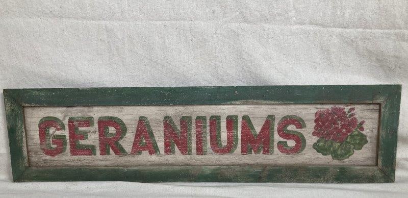 Country Painted Wood Sign, "Geraniums'': Hand-painted on wood with vibrant green and purple lettering against an off-white background, this charming sign reads "Geraniums." Measures 8'' x 32''. Worn surface otherwise good condition. Shipping