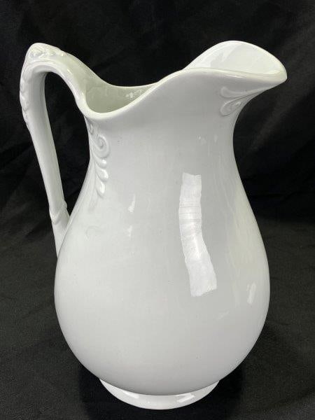Ironstone Pitcher: Elegant ironstone pitcher featuring raised floral decoration and a classic, flowing form. Marked by the maker on the base. Measures approx. 12''H x 9''W. Some crazing present. Shipping available.