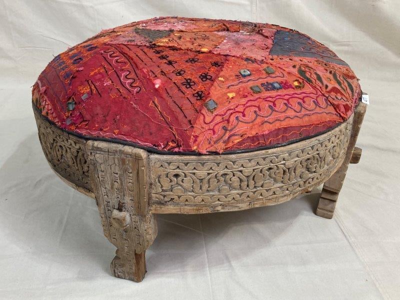Carved Circular Indonesian Ottoman: Striking circular ottoman featuring intricate hand-carved detailing around the wooden base and a vibrant multicolored upholstered top. Measures approx. 14''H x 32'' in diameter. Multiple repairs to th