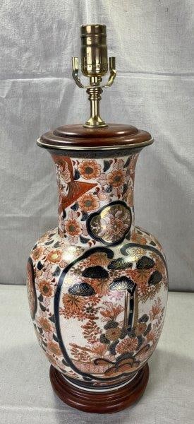 Japanese Imari Porcelain Lamp: Features traditional hand-painted Imari floral motifs with gilt detailing. Accented with wood and brass elements at the base and top. Measures approximately 21 1/2''T x 8 1/2'' in diameter. Surface sh