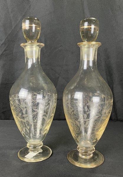 Pair of Hand-Blown and Etched Glass Wine Decanters: Each features intricate swirled leaf etching with gilded accents on the rims, stoppers, and bases. Elegant, hand-crafted forms with matching stoppers. Each decanter measures approximately 12 3/4''T x