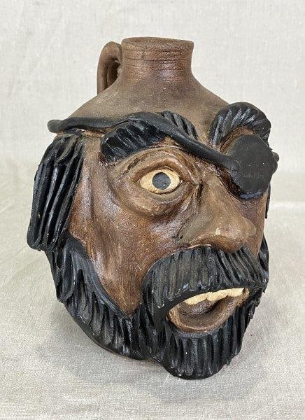 Kim T. Black Pirate Face Jug: Folk art face jug by potter Kim T. Black, featuring a whimsical pirate motif with black beard, eye patch, and bisque eye and teeth. Finished in a warm brown color with detailed beard. Measures approxi