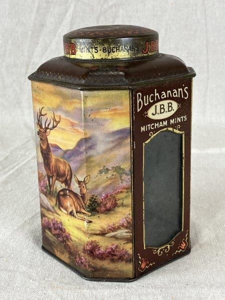 Buchanan's J.B.B. Mints Metal Tin: A Buchanan's J.B.B. Mints metal tin of octagonal form, with sides featuring elk, cattle, and a scenic valley with a lake, a glass front, and a decorated lid. Measures approximately 7" H x 4¼" W x