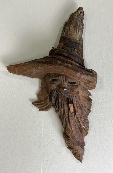 Folk Art Carved Face: A folk art carved face of a man smoking a pipe and wearing a hat, with finely carved details and a warm patina. Measures approximately 10 3/8" H x 6 1/4" W x 2" D. Good condition.