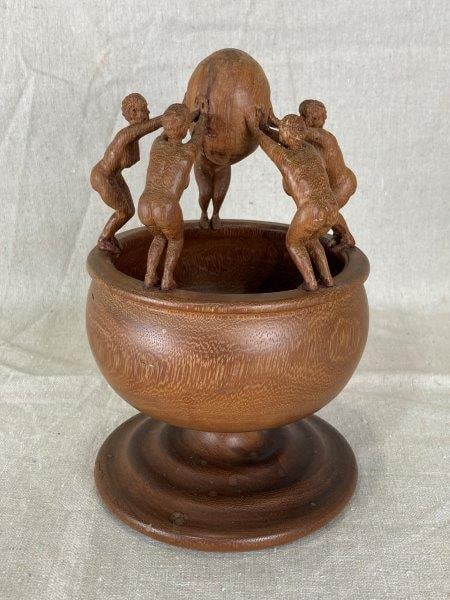 Art Deco Styled Carving: Intricately carved figure with detailed motifs along the rim, finished in a warm brown tone. A striking decorative piece in the Art Deco style. Measures approximately 9'' H x 5 3/8'' W x 3 3/8'' D. Go