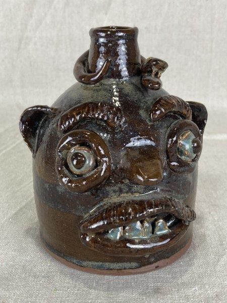 Larry Kyzer Face Jug, South Carolina: Folk art face jug by South Carolina potter Larry Kyzer who passed away in May of 2025, featuring a boldly applied snake motif and a rich dark glaze with striking color variation in the eyes and teeth.