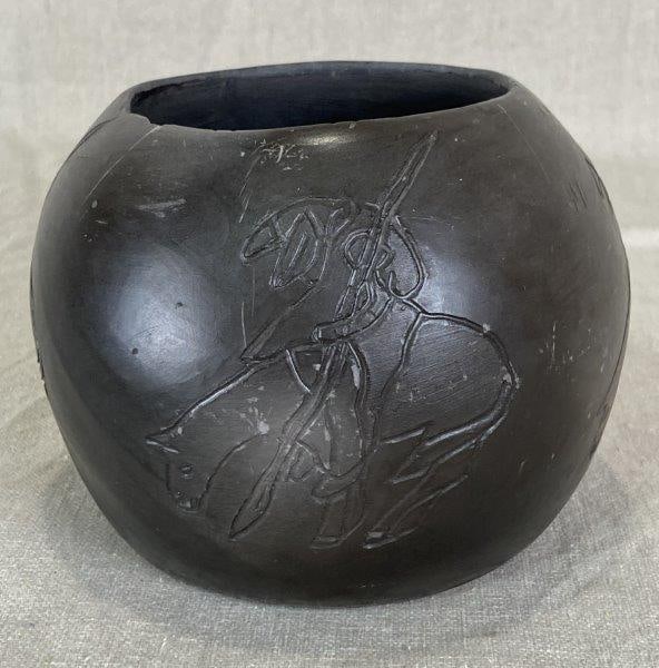 Louise Bigmeat Maney Cherokee Blackware Pottery: End of Trail, incised decoration depicting a Native American figure on horseback encircling the vessel, signed to base. Measures approximately 4" H x 4 5/8" in diameter. Good condition with a small ch