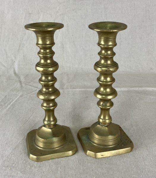 English Brass Candlesticks: Classic form with warm patina, crafted in solid brass with traditional English styling. Each measures approximately 8" H x 3 1/8" W x 3 1/8" D. Good condition with minor oxidation spots consistent wit