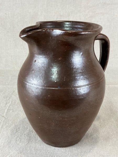 Georgia Stoneware Pitcher: Traditional Southern stoneware pitcher finished in a rich Albany slip glaze with an applied loop handle. Measures approximately 8" H x 7" W x 5" D. Good condition with light wear consistent with age.