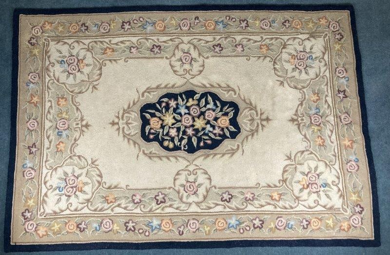 Floral Hooked Rug: Featuring a bold black border with an ivory field, this charming hooked rug is centered by a vibrant floral medallion. Measures approx. 69'' x 101''. Some repairs, has discoloration.