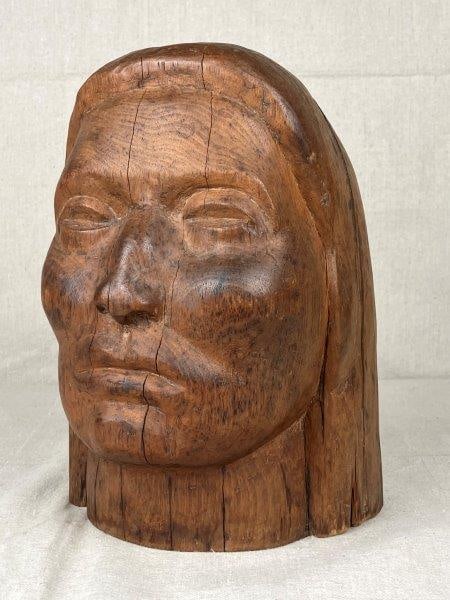 Carved Bust of Native American: Finely carved wooden bust with detailed facial features and a warm patina. Measures approximately 10 3/8'' H x 7'' W x 7'' D. Condition: Good, with natural splits in the wood.