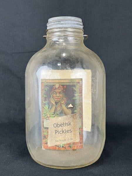 Black Americana Obelisk Pickle Jar: Glass pickle jar featuring illustrated African American advertising labels for the Obelisk Pickles brand, printed by Beach & Sherwood. Measures approximately 12 1/4" H x 6" in diameter. Labels display