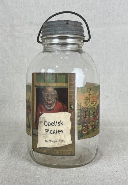 Black Americana "Obelisk Pickles" Glass Jar: Produced by Beach & Sherwood Packers, New York, this rare glass jar features advertising illustrations of notable African American figures encircling the vessel for the historic Obelisk pickle brand. 