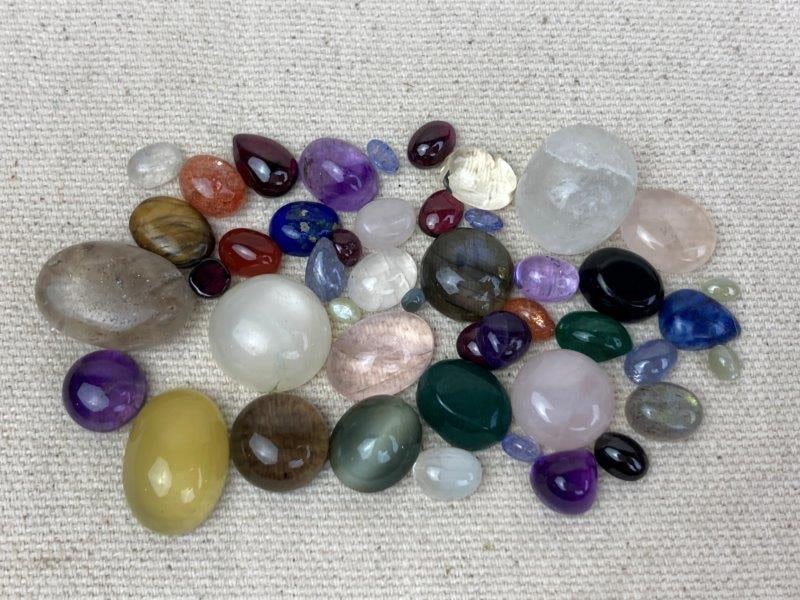 Lot of Polished Cabochon Gemstones: Collection of polished cabochon gemstones including jade, moonstone, quartz, and amethyst, presented in various shapes and sizes and ready for settings. In good condition.