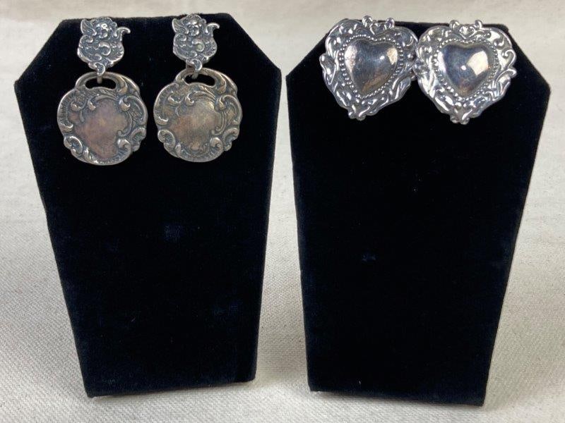 Two Pairs of Sterling Silver Art Nouveau-Style Earrings: Including one pair of round luggage tag-style earrings with cherubs above scrolling round attachments, marked T Foree Sterling on the reverse, together with a pair of heart-shaped earrings adorned wit