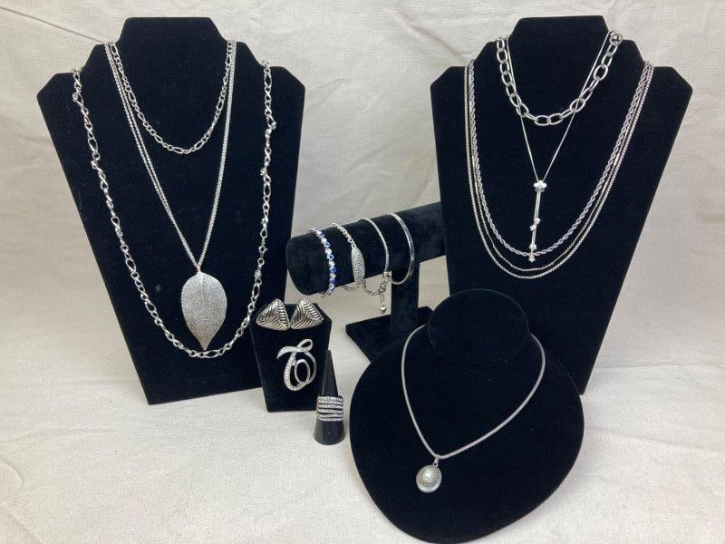 Assorted Lot of Silver-Tone Jewelry: A diverse collection of silver-tone jewelry including seven necklaces, four bracelets, one pair of wavy triangle earrings, a brooch adorned with clear crystal rhinestones, and a multi-row chevron ring