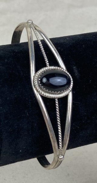 Sterling Silver and Onyx Cuff Bracelet: Elegant sterling silver cuff bracelet featuring an oval onyx cabochon set in a detailed rope-style bezel. Measures approximately 2 1/2" x 1 5/8". In good condition with light wear consistent with age