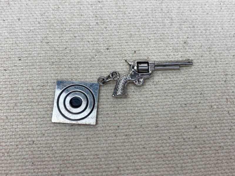 Sterling Silver Revolver and Target Charm: Two-piece sterling silver charm set featuring a detailed revolver and target motif. The revolver measures approximately 1 1/4" long. Stamped Sterling on clasp. In good condition with light wear consis
