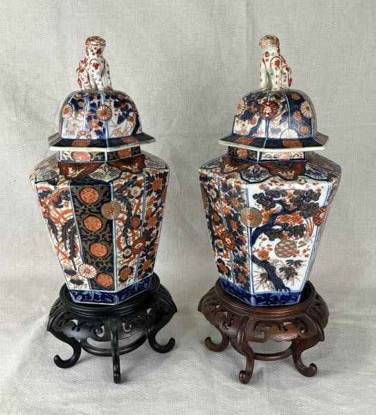 Pair of Meiji Period Imari Covered Jars with Dog Finials: A fine pair of Imari porcelain covered jars, each surmounted by a dog-form finial and painted with characteristic floral and geometric motifs in rich polychrome enamels. One measures approximately 15"