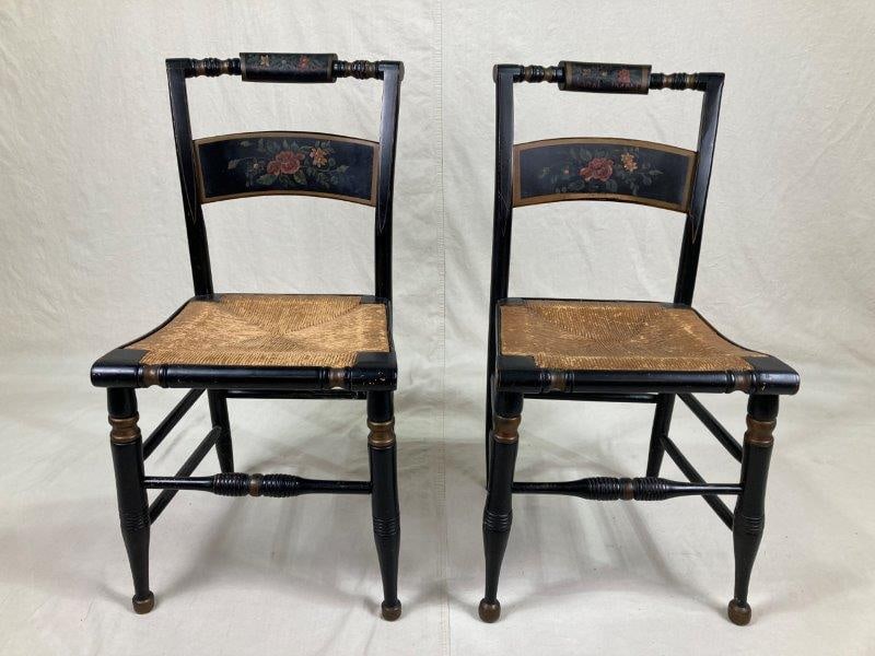 Pair of Hitchcock Chairs: Two classic Hitchcock chairs featuring a hand-painted splat decorated with a floral motif, woven seat, and turned legs with stretchers. The chair shows a warm aged patina.One measures approximately 34