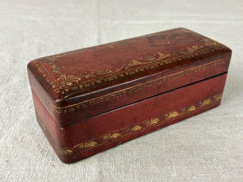 Gold-Tooled Leather Box: Refined leather box in rich sienna-red tones, decorated with a delicate leafy design in gold tooling, showcasing craftsmanship and elegant detailing. Measures approximately 2" H x 5 1/8" W x 2" D and