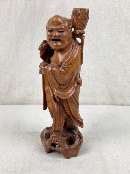 Chinese Arhat Statue: Finely hand-carved wood statue depicting an Arhat, shown with a large plant upon his back and holding a bat in one hand, symbolizing prosperity and good fortune. Features a warm aged patina. Measures 