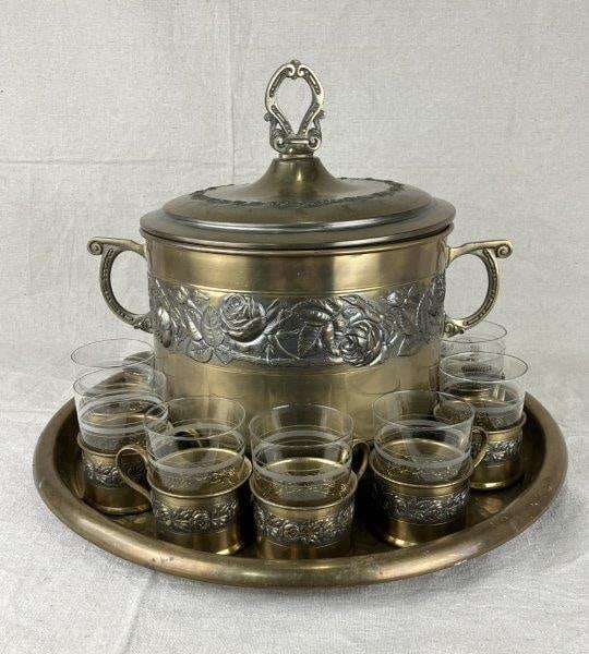 Brass Punch Set: Distinctive brass punch set featuring repoussé rose motifs and a hammered metal tray, accompanied by twelve brass cups. Measures approximately 14" H x 16" in diameter. Some brass components are m