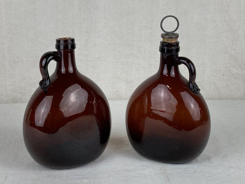 Pair of 19th Century Decanters: Elegant pair of amber glass decanters, each with applied handles and fine proportions. The decanter with cork measures approximately 8 5/8" H x 5 3/8" W x 3 1/4" D. Good condition, with one missing it