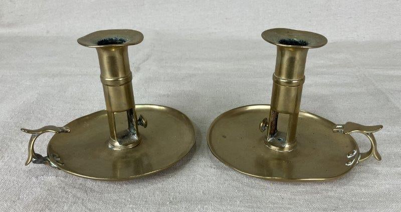 Pair of Brass Candlesticks: Elegant pair of brass candlesticks featuring a traditional adjustable push-up design, crafted with a warm reflective finish. One measures approximately 4 5/8" H x 5 3/8" in diameter. Both show some pa