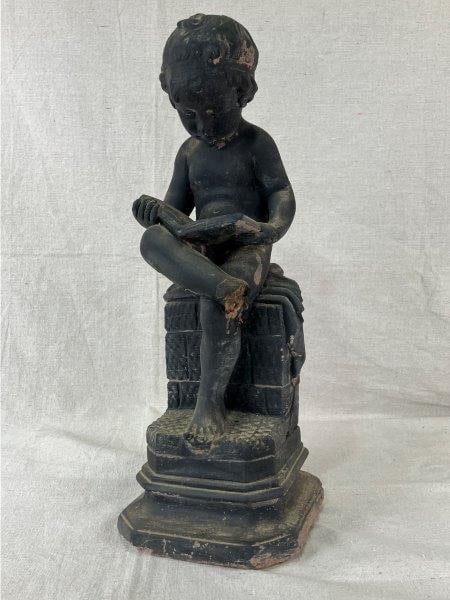 Cast Statue of a Seated Boy: Charming cast statue depicting a boy seated while reading, finished in painted dark tones. Measures approximately 16 3/4" H x 6" W x 6" D. Some wear throughout with loss to one foot.