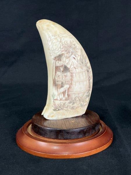 Scrimshaw Whale’s Tooth, Late 18th Century: A finely detailed scrimshaw whale’s tooth with three-color incised decoration depicting an early scene of a native leaning on a barrel smoking a pipe. Accompanied by an old newspaper clipping li