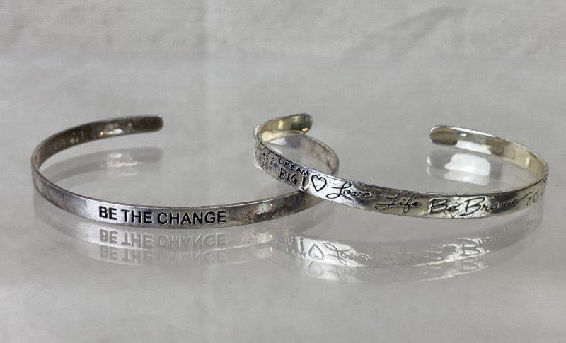 Group of Sterling Silver Cuff Bracelets: Collection of two sterling silver bangles, one engraved with inspirational phrases throughout and the other inscribed "Be the Change". Both stamped 925 LA TH and crafted with a polished silver finish.