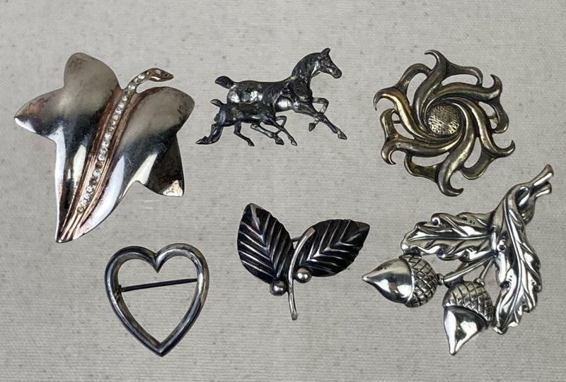 Six-Piece Sterling Silver Brooch Collection: Charming collection of six sterling silver brooches showcasing varied motifs including horses, leaves, acorns, a heart, and curved abstract forms. Each piece displays fine detailing and vintage charac