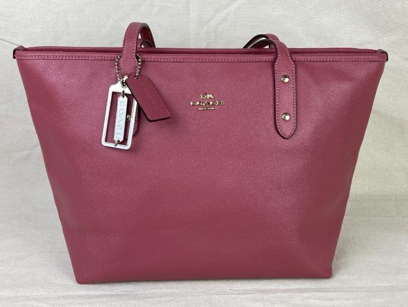 Coach City Zip Tote: Chic Coach City Zip Tote crafted in pink pebbled leather with gold-tone hardware, including a signature Coach charm suspended from the strap. Features a zip-top closure and a canvas-style interior wit