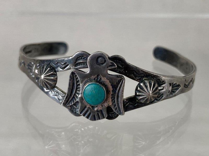 Vintage Navajo Sterling Silver Cuff Bracelet: Vintage Navajo sterling silver cuff bracelet featuring a turquoise cabochon framed by an engraved thunderbird motif and traditional tribal designs. Marked Sterling. Measures approximately 2" in diamet