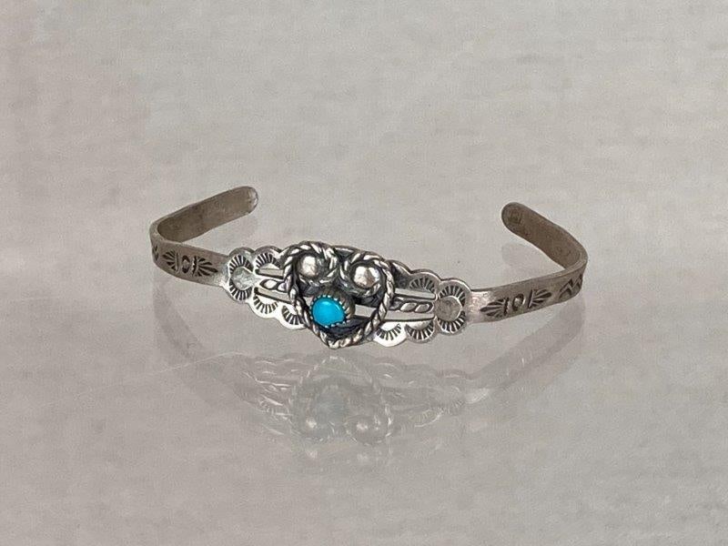 Native American Sterling Silver and Turquoise Cuff Bracelet: Delicate Native American sterling silver cuff bracelet featuring a small round turquoise cabochon framed by a rope and heart motif on a decorated band. Stamped Sterling on the interior. Measures appro
