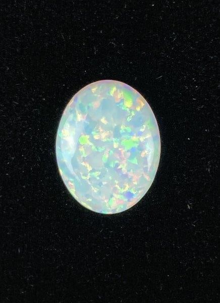 Cultured Opal Cabochon: Iridescent oval cultured opal cabochon displaying a vivid play of prismatic color with shifting tones of blue, green, and pink. Measures approximately 3/4" high x 5/8" wide x 1/8" deep. In good condit