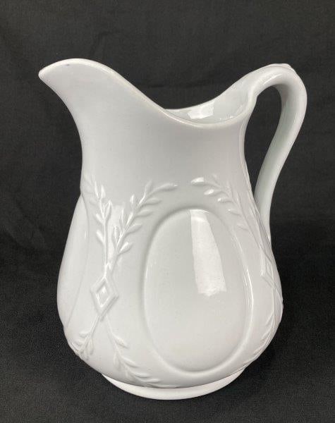 Ironstone Pitcher: Elegant ironstone pitcher featuring a raised foliage motif with geometric accents and a round medallion on the body. The handle displays a refined leaf motif design. Stamped and made by Powell & Bisho