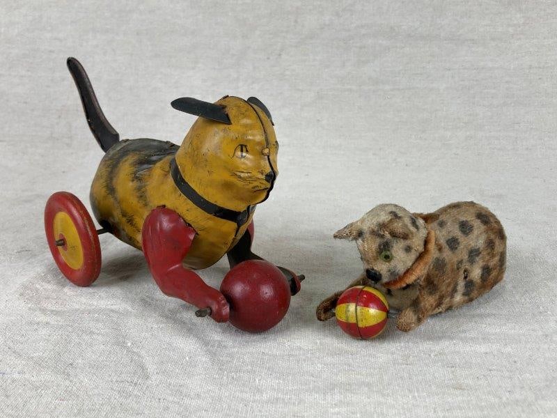 Tin Wind Up Cat Toy Pair: Charming pair of tin wind-up cat toys, one featuring a faux fur–covered body and the other a tin lithographed form, each depicted chasing a ball and mounted on wheeled bases. Delightful examples