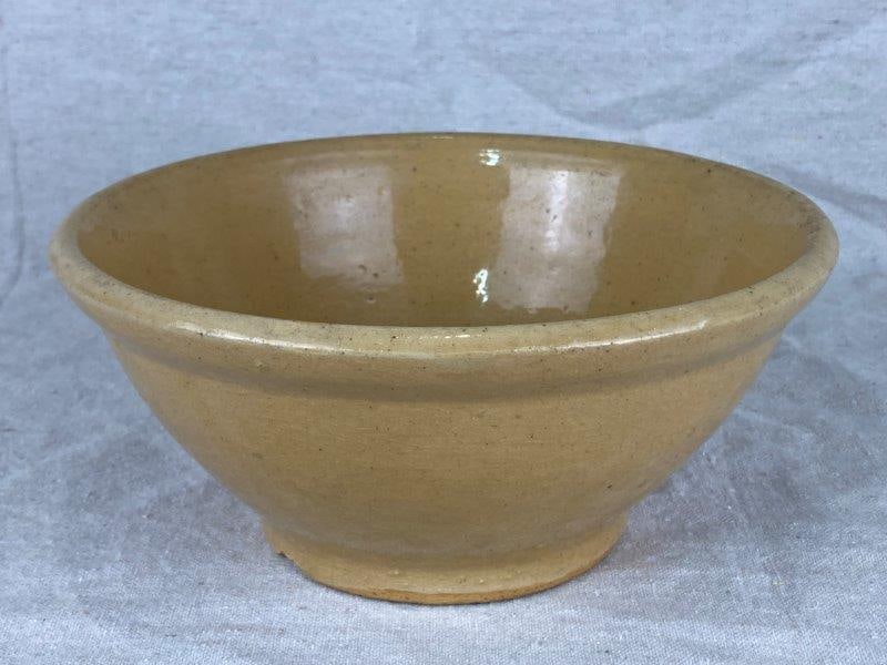 Yelloware Mixing Bowl: Charming yellow ware bowl in a classic utilitarian form with a molded rim and surface crazing. Measures approximately 4 1/4'' H x 9 1/8'' W x 9 1/8'' D. Good condition with minor wear and light loss a