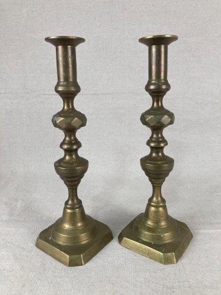 Pair of Brass Candlesticks: Elegant pair of brass candlesticks featuring rich golden tones and gracefully undulating forms throughout. One measures approximately 11 7/8" H x 3 3/4" W x 3 3/4" D. Some minimal spotting consistent