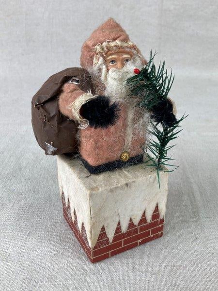 Vintage Santa and Chimney Figurine: Charming mixed-material holiday figurine featuring Santa climbing down a chimney, crafted with fabric, paper, faux greenery, and other decorative materials. Displays distinctive handmade character and