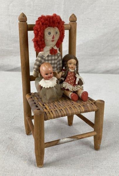 Miniature Country Chair with Vintage Dolls: Charming miniature country chair in traditional form with a warm light patina, accompanied by vintage fabric and mixed-material dolls. Measures approximately 8" H x 3 3/4" W x 3 3/4" D. Some age-appro