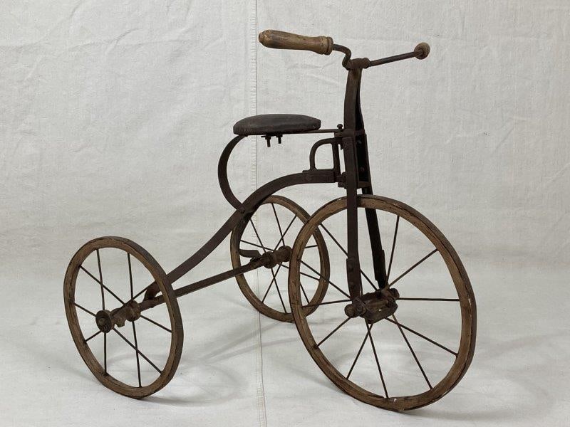 Vintage Metal Tricycle: Classic vintage tricycle featuring turned wood handles, a leather seat, and wooden wheels with a warm aged patina. Measures approximately 25 7/8'' H x 20'' W x 29'' D. Age-appropriate wear.