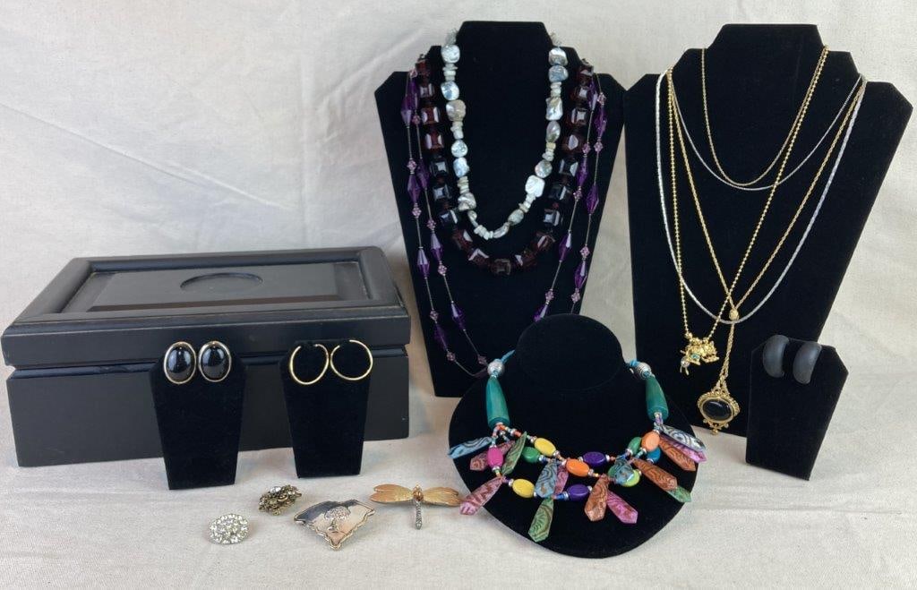 Jewelry Box with Vintage Jewelry Assortment: Jewelry box filled with a variety of vintage jewelry pieces in assorted forms and designs. A standout item is an Estée Lauder piece featuring a central green-toned acrylic stone framed in gold to
