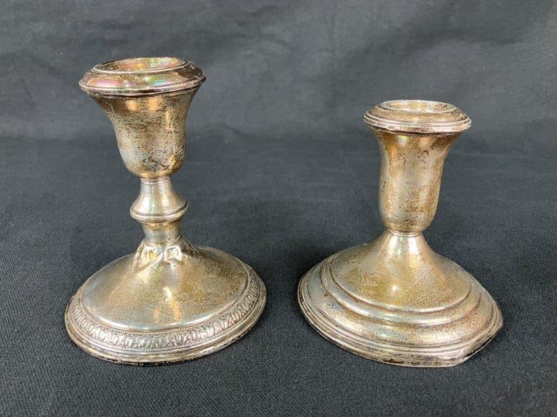 Sterling Silver Candlesticks: A pair of sterling silver candlesticks, each crafted in weighted or reinforced sterling construction. One example measures approximately 4 5/8" H x 3 5/8" in diameter. Exhibits bends, tarnishing, and