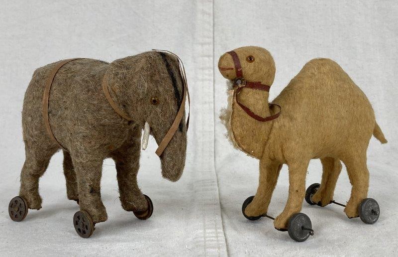 Antique Animal Pull Toys: Two charming mohair pull toys including a camel on metal wheels and an elephant on cork and metal wheels, both with glass eyes and attributed to Steiff. Each displays a worn aged patina. The camel mea