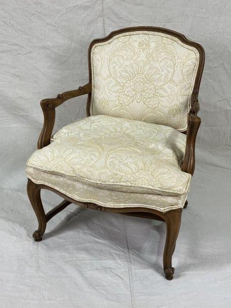 Louis XV Style Armchair: A Louis XV-style armchair featuring a decoratively carved wood frame with cabriole legs and elegant damask upholstery complemented by a matching down cushion. The frame displays a warm aged patina. Me