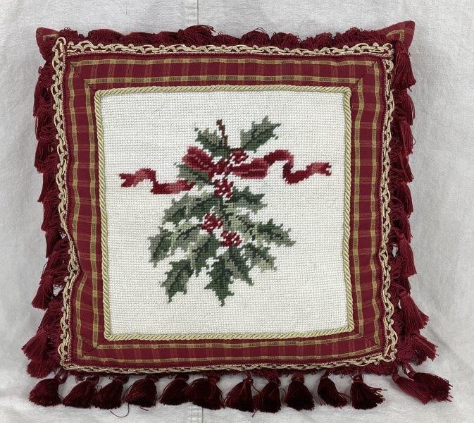 Christmas Needlepoint Pillow: Festive needlepoint pillow featuring holly leaves, berries, and a red ribbon, accented with gold cord trim and red tassels on the edges. Measures approximately 15 1/4" H x 15 3/4" W x 4 3/4" D. Good c
